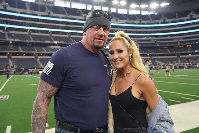 Mark William Calaway in a grey skull caps and navy blue t-shirt with his wife Michelle McCool in a black thin-laced top.